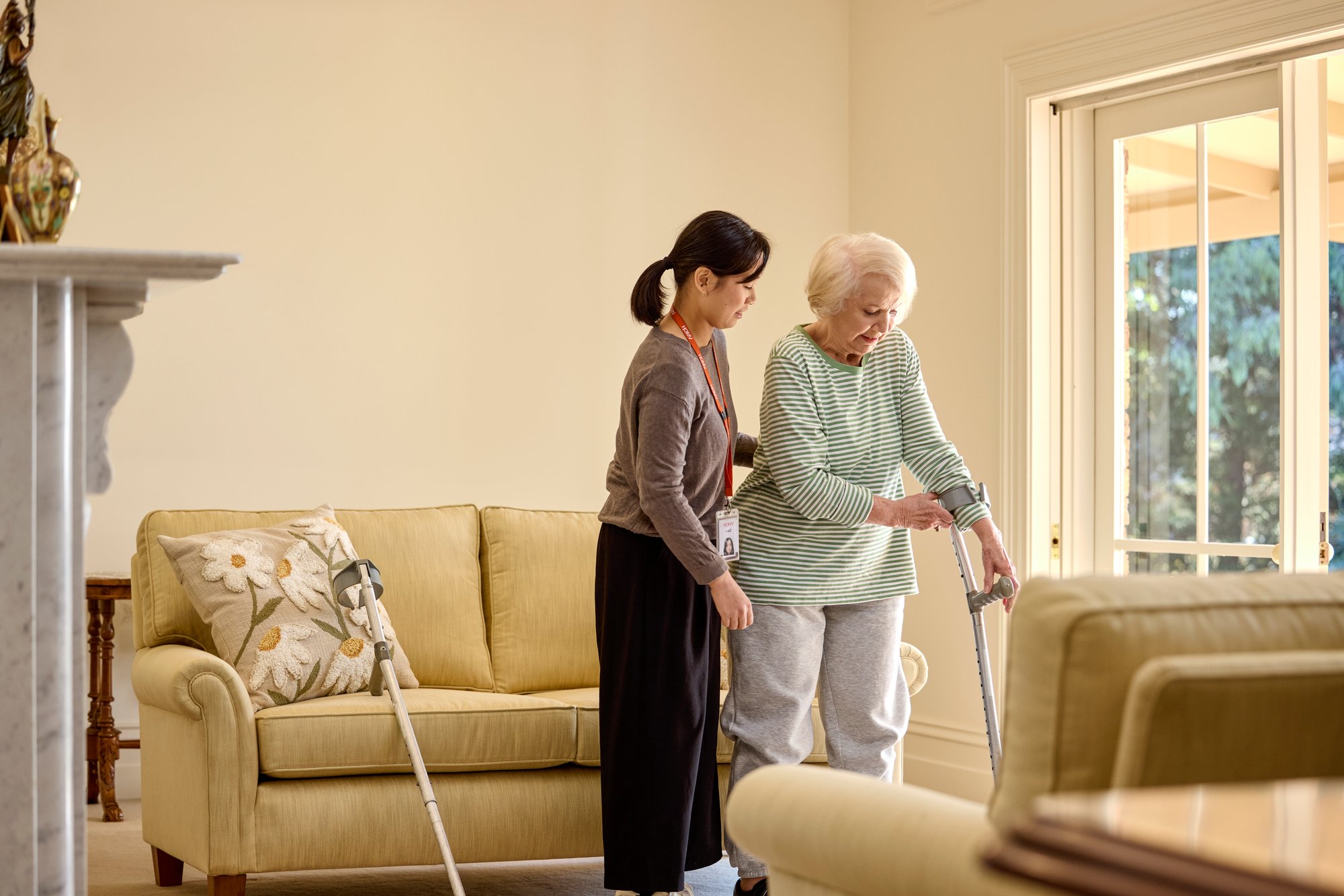 A carer helping an older woman use crutches.