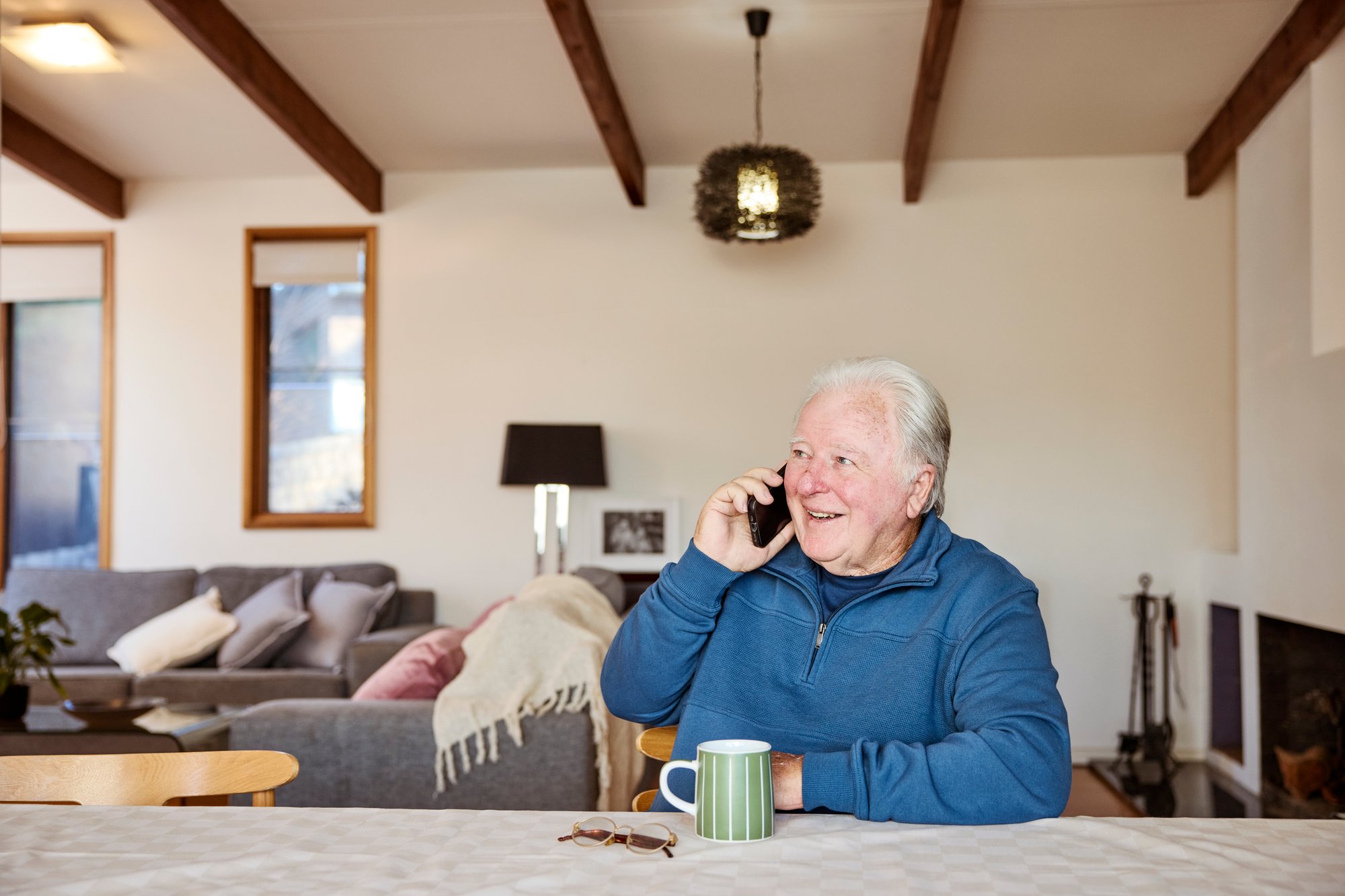 An older man sitting at the table on his phone and smiling