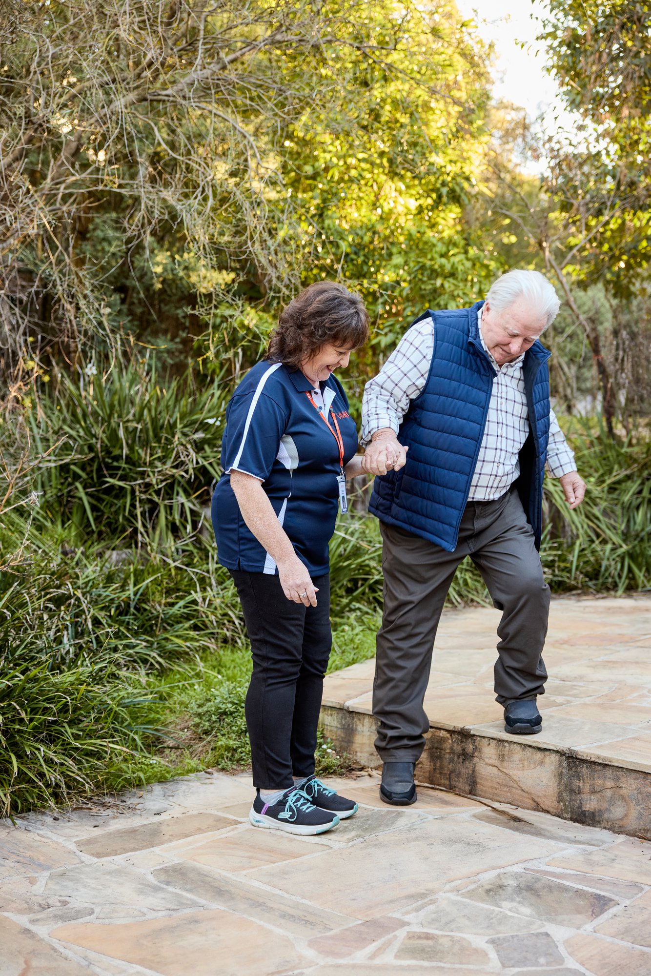 A home care support worker helping an older man step down an outdoor step