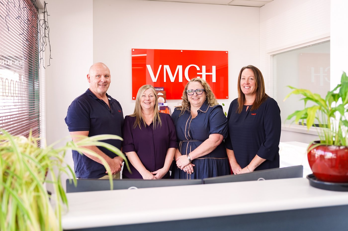 Four people standing in an office, in front of an orange sign.