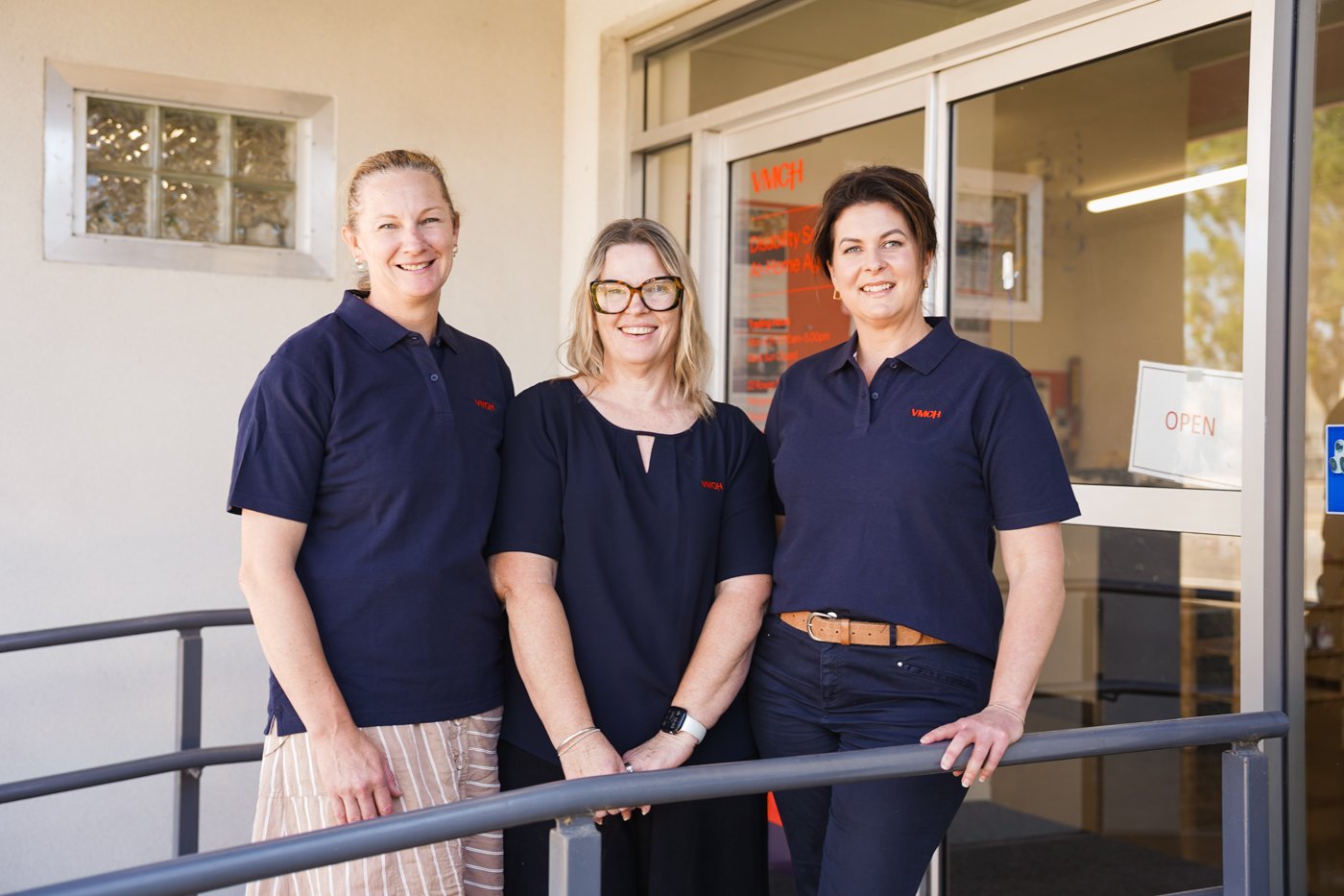 Three women posing professional and smiling outside a building.