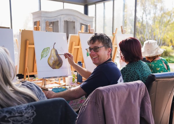 A man painting a pear on a canvas.