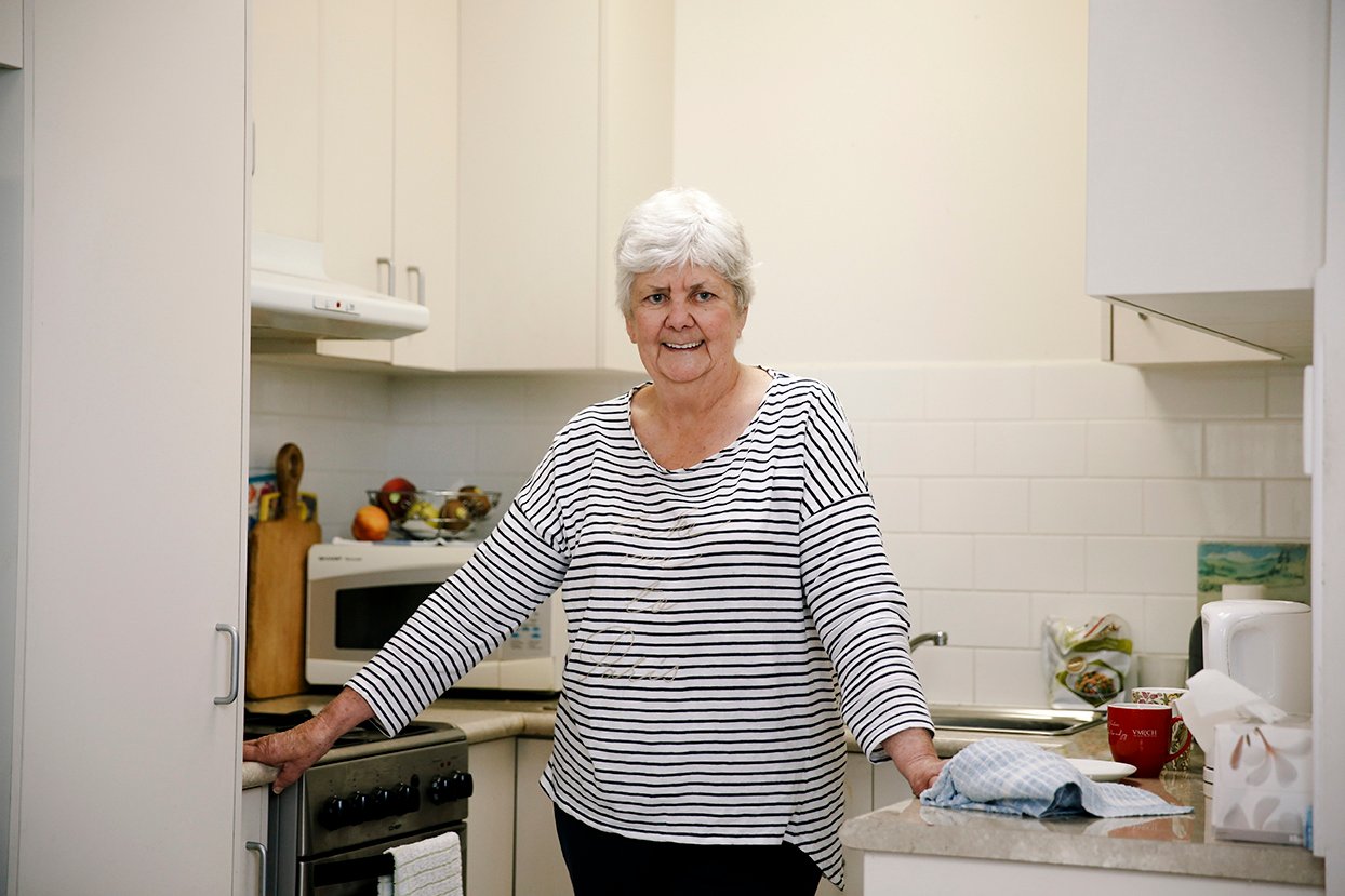 An older woman stands in her kitchen