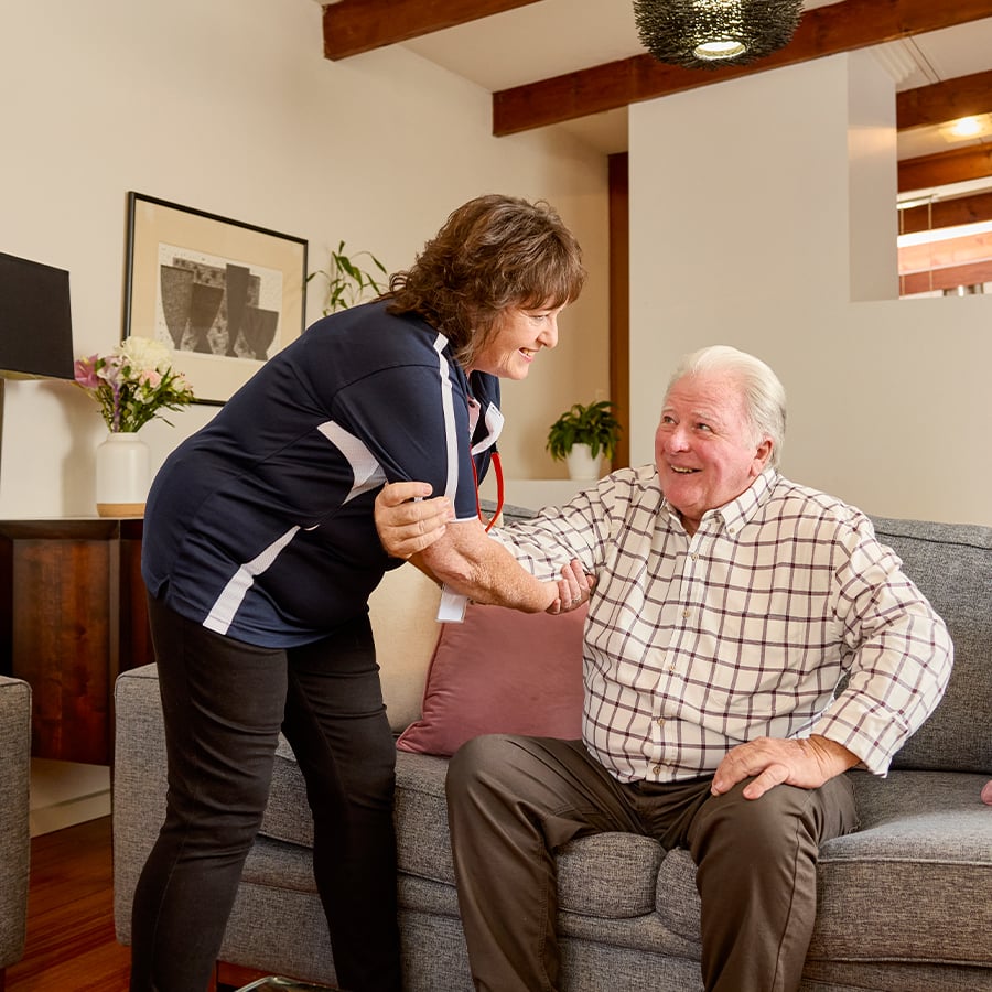 VMCH aged care staff member assisting a resident to stand from the couch, providing supportive and compassionate in-home care.