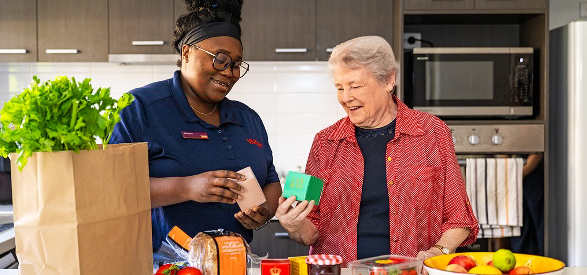 A female VMCH support worker helping an elderly woman in her kitchen unpack groceries