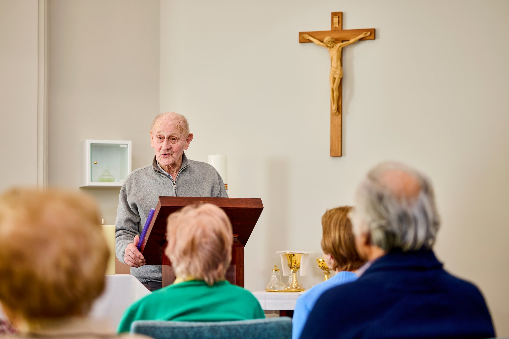 An elderly man reading from the bible in front of a group of people during a Catholic service