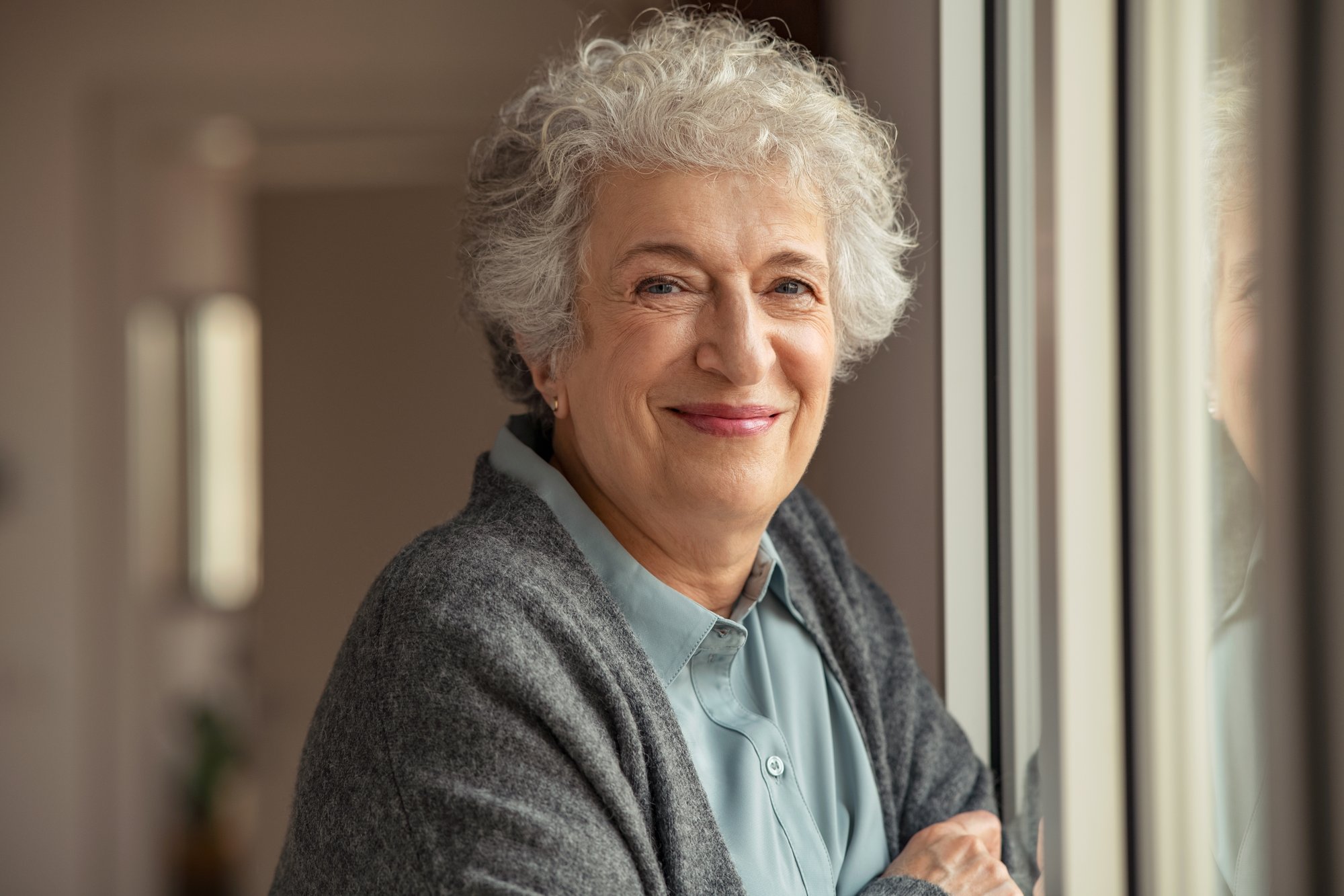 An old woman with grey hair, standing by the window.